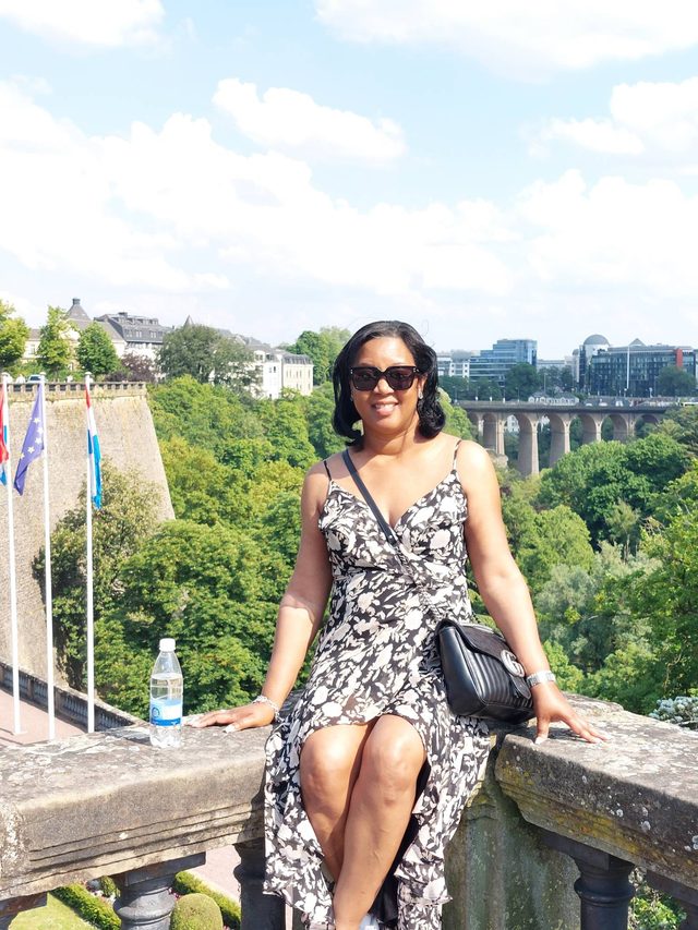 Tamica sitting on a stone wall above a green valley in Luxembourg