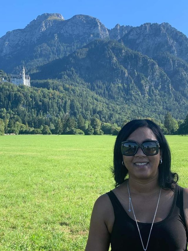 Tamica in a meadow with Neuschwanstein Castle and the Alps behind her