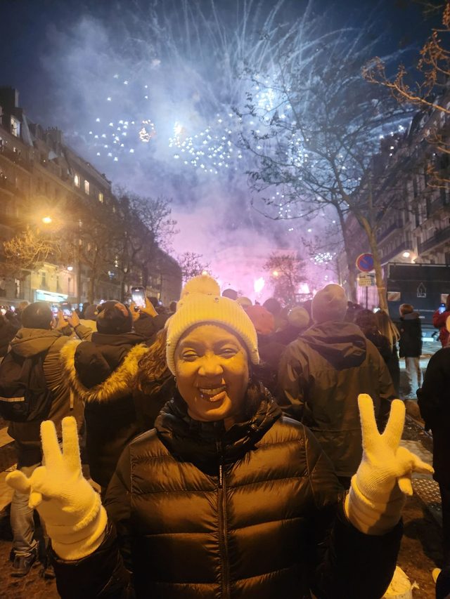 Tamica smiling in a Paris street as fireworks light up the sky