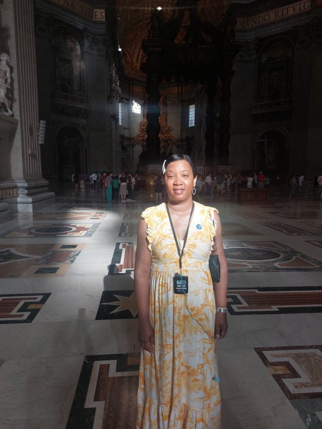 Tamica in a yellow sundress inside St. Peter's Basilica as sunlight falls across the marble floor